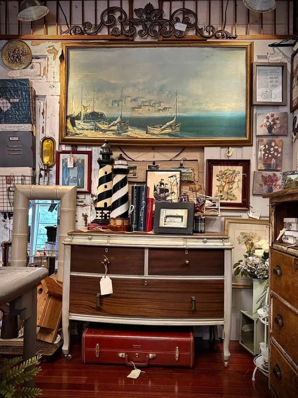 Vintage dresser styled with nautical art, lighthouses, books, and a red suitcase