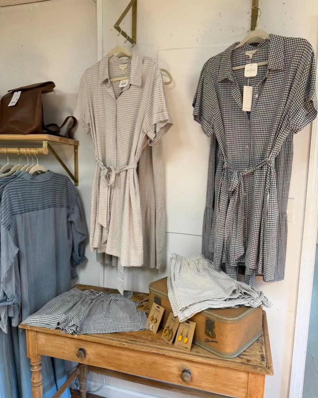 Women's boutique display with gingham dresses, accessories, and a vintage suitcase