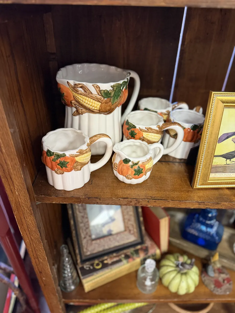 White ceramic pitcher and matching mugs painted with pumpkins and corn on a wood shelf at Vintage 72