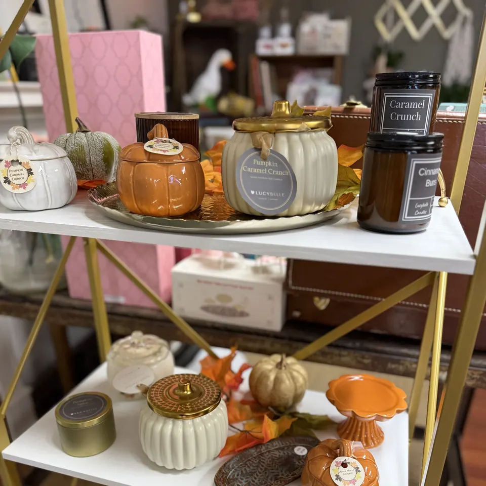 Pumpkin-shaped Pumpkin Caramel Crunch candle jars and a Lucybelle soy candle on a white shelf at Vintage 72