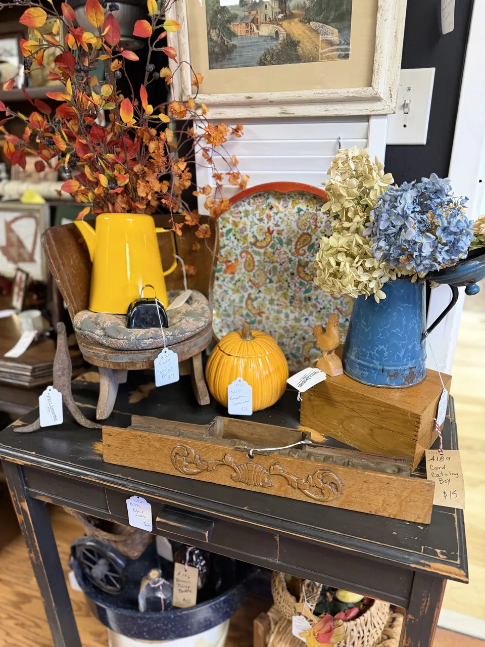 Fall display with a yellow enamel coffeepot, blue enamel pitcher, dried hydrangeas, and a ceramic pumpkin at Vintage 72